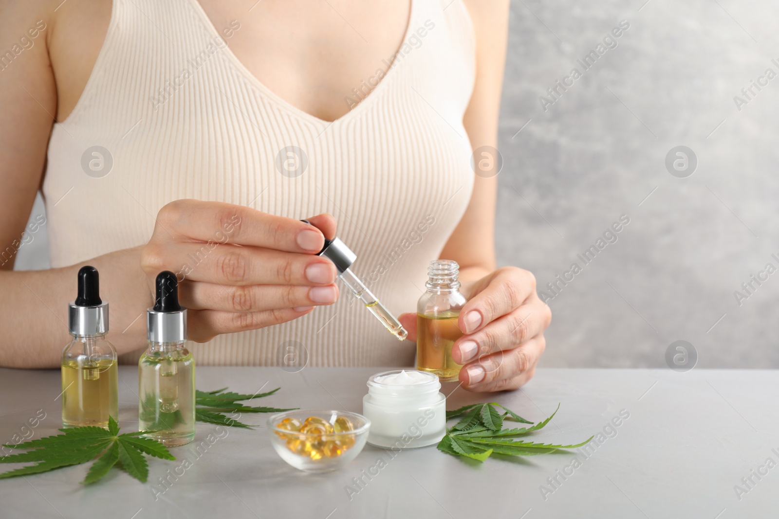 Photo of Woman dripping THC tincture or CBD oil into cream at light stone table, closeup