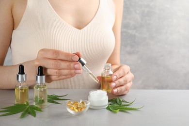 Photo of Woman dripping THC tincture or CBD oil into cream at light stone table, closeup
