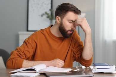 Photo of Overwhelmed man suffering from headache at table indoors