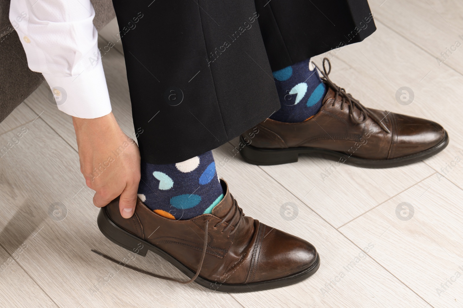 Photo of Man with colorful socks putting on stylish shoes indoors, closeup