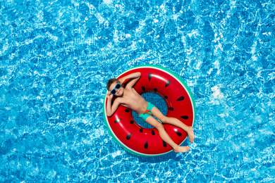 Image of Cute little boy with inflatable ring in swimming pool, top view. Summer vacation