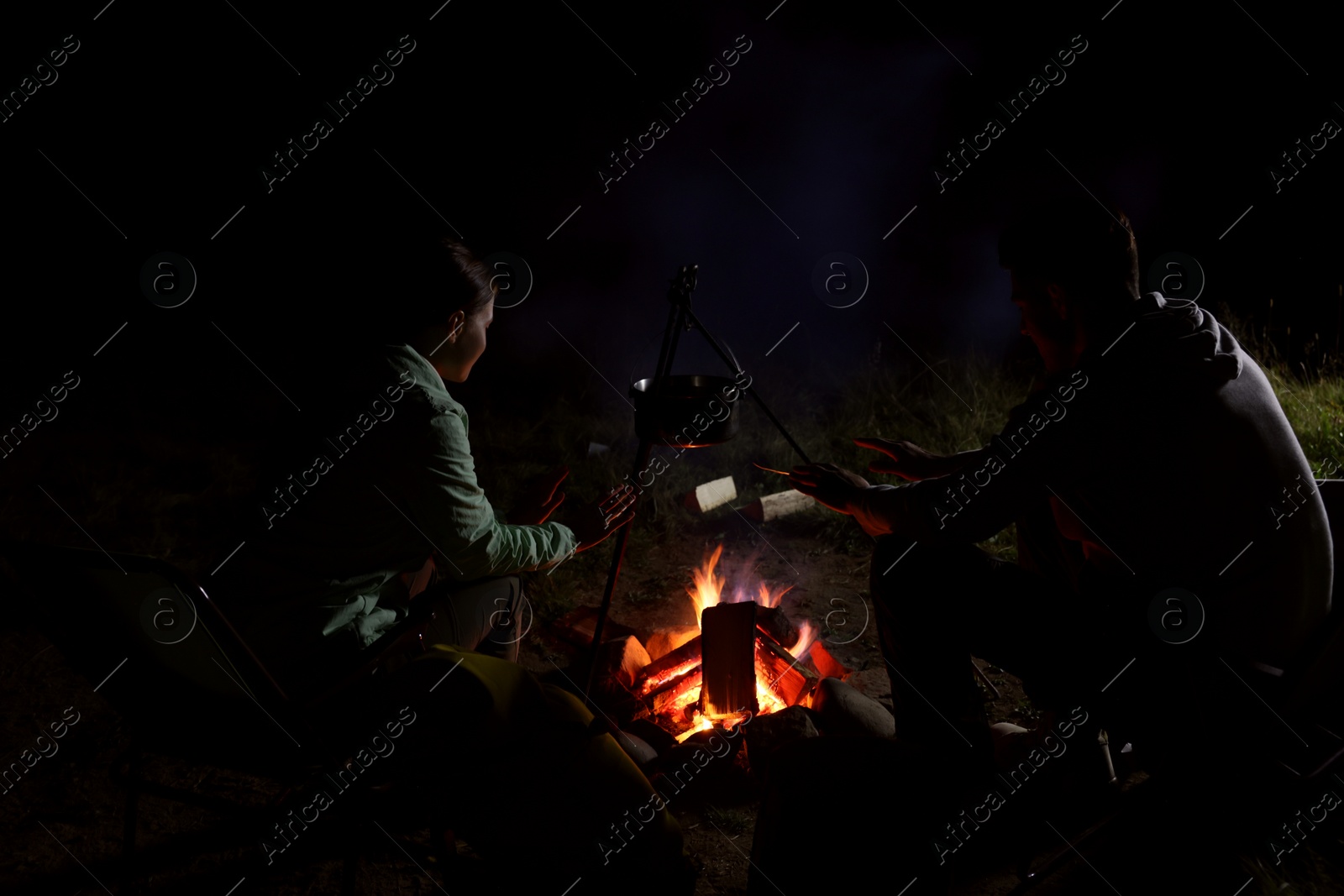 Photo of Couple sitting near bonfire in camp at night