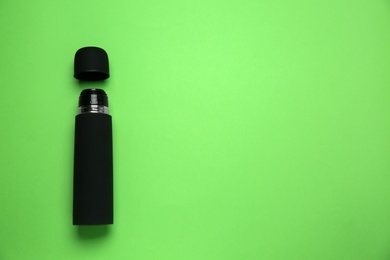 Photo of Black thermos and cup on green background, flat lay. Space for text
