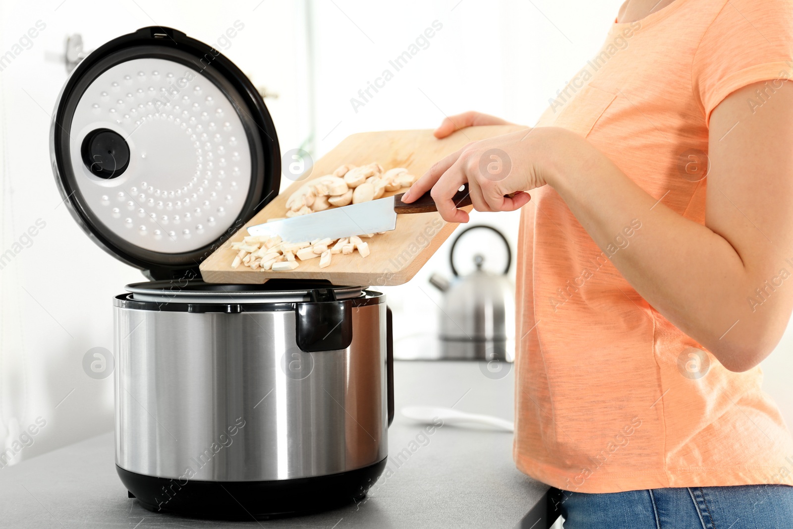 Photo of Young woman preparing mushrooms with modern multi cooker in kitchen, closeup