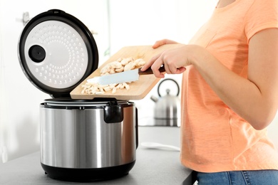 Young woman preparing mushrooms with modern multi cooker in kitchen, closeup