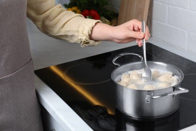 Photo of Woman cooking dumplings in saucepan with boiling water on cooktop, closeup