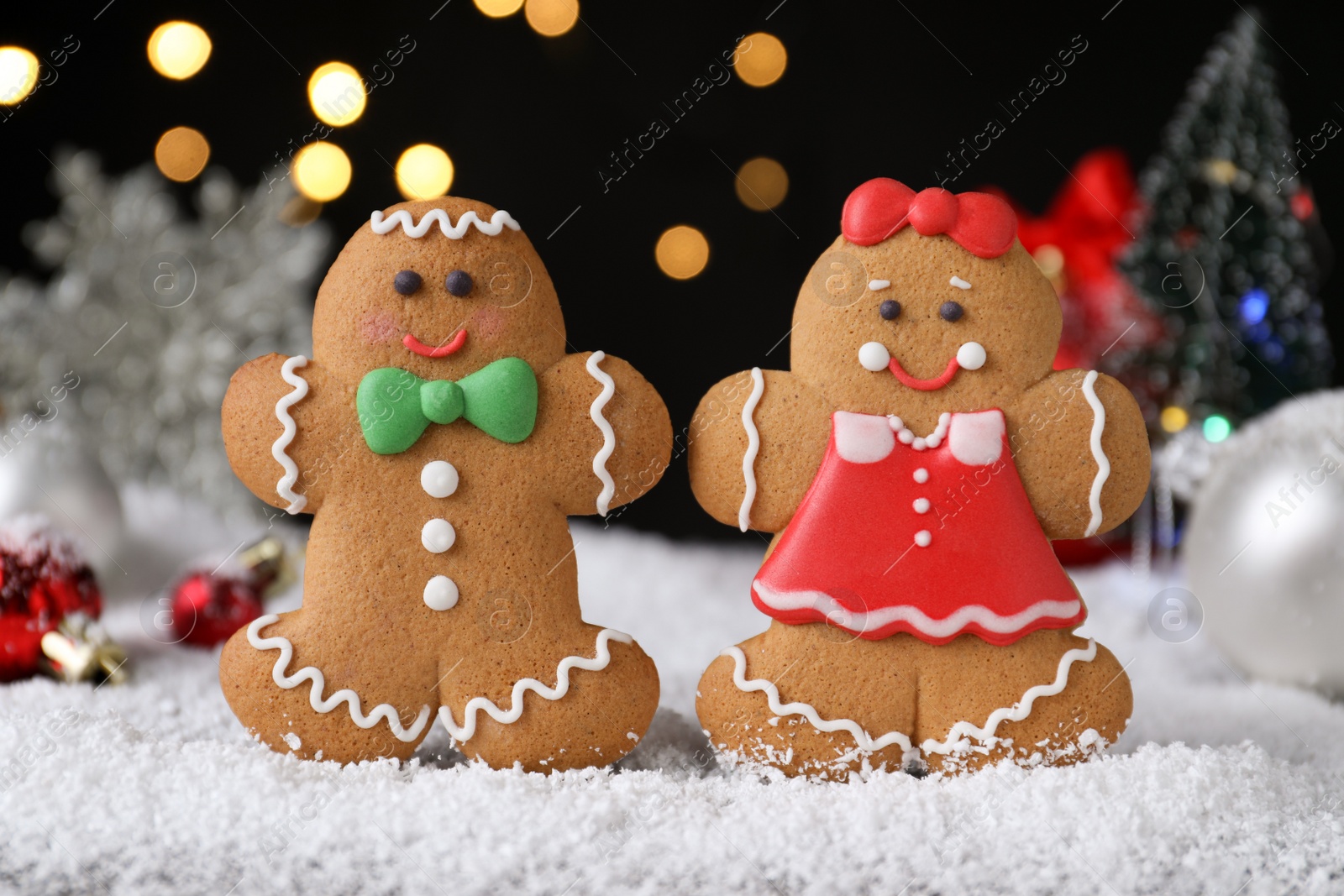 Photo of Gingerbread people on snow against festive lights, closeup