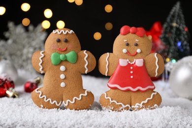 Photo of Gingerbread people on snow against festive lights, closeup