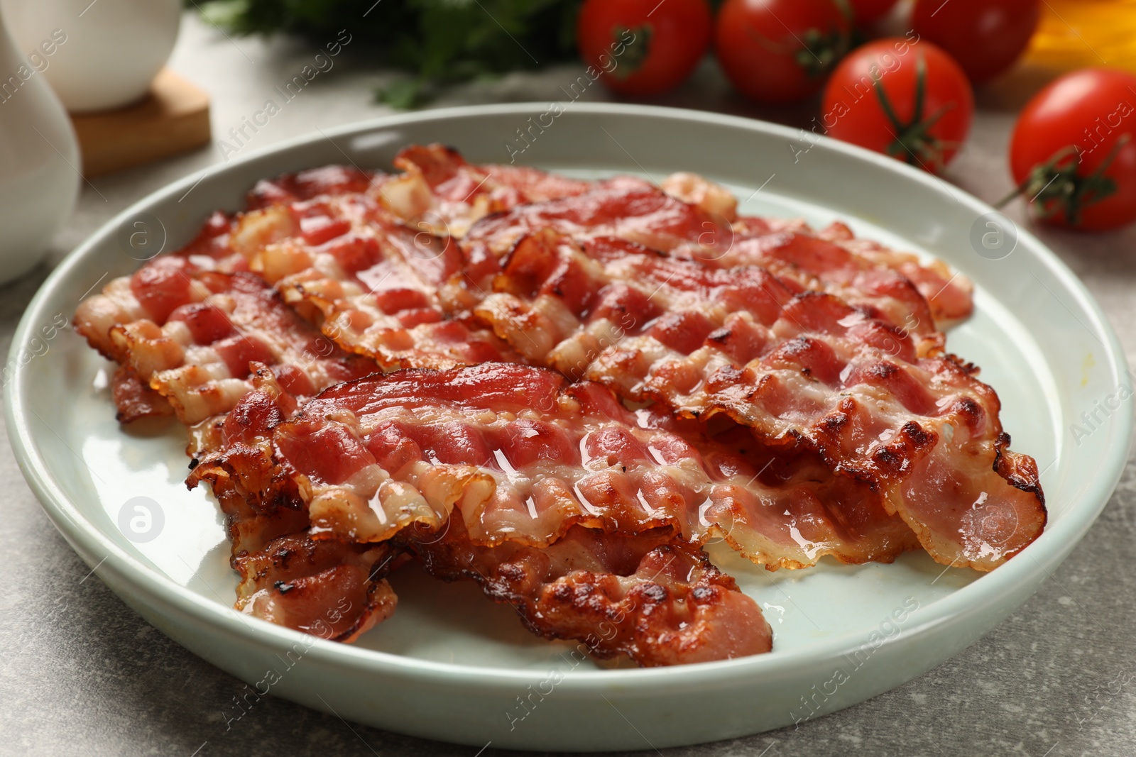 Photo of Plate with fried bacon slices on grey textured table, closeup