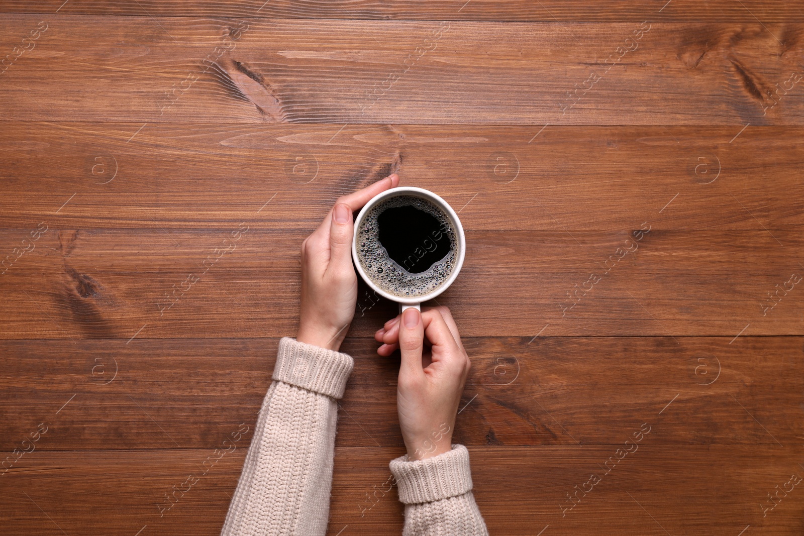 Photo of Woman with cup of coffee at wooden table, top view