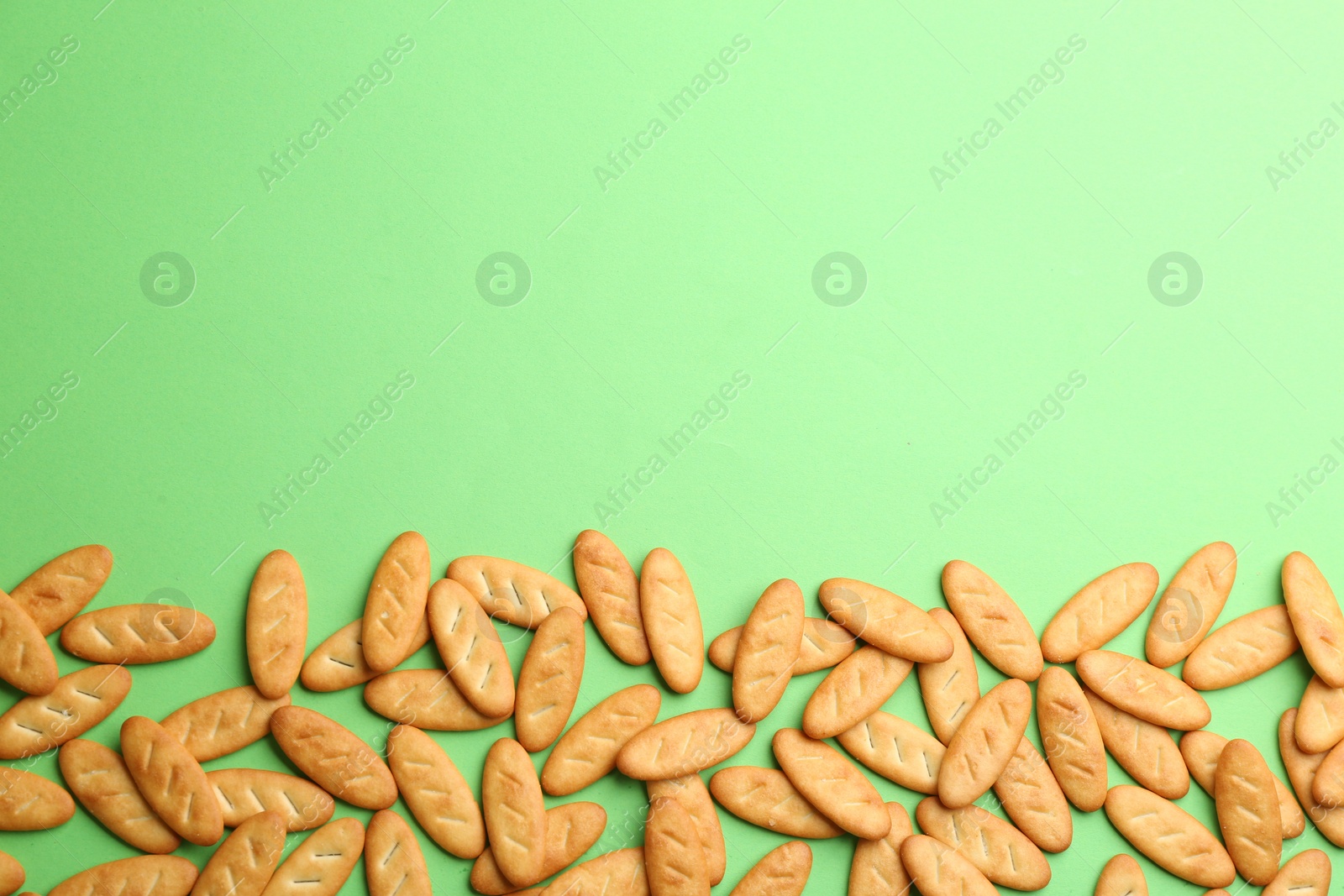 Photo of Delicious crackers on light green background, flat lay. Space for text