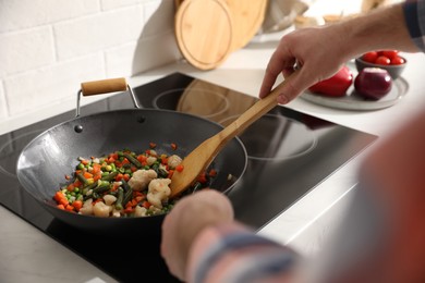 Photo of Man stirring mix of fresh vegetables in frying pan, closeup