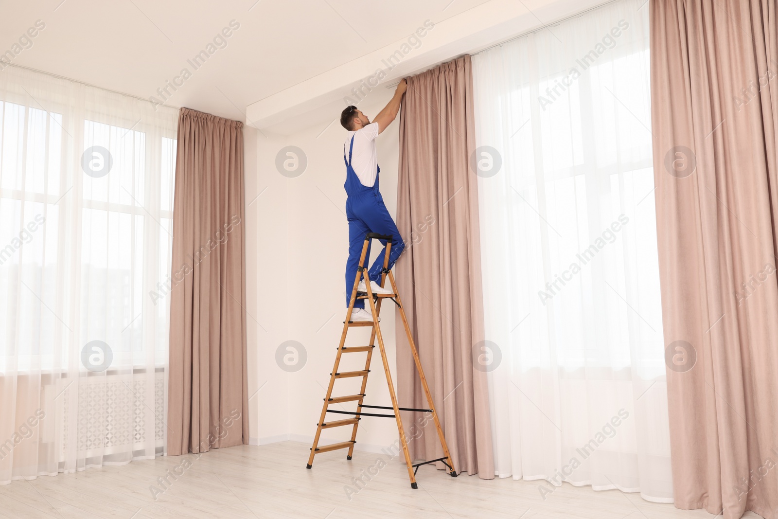 Photo of Worker in uniform hanging window curtain indoors