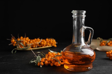 Photo of Ripe sea buckthorn and jug of essential oil on black table. Space for text