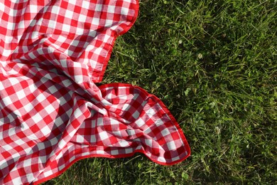 Photo of Checkered picnic tablecloth on fresh green grass, top view. Space for text