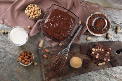 Photo of Bowl of chocolate cream, whisk and ingredients on grey textured table, flat lay