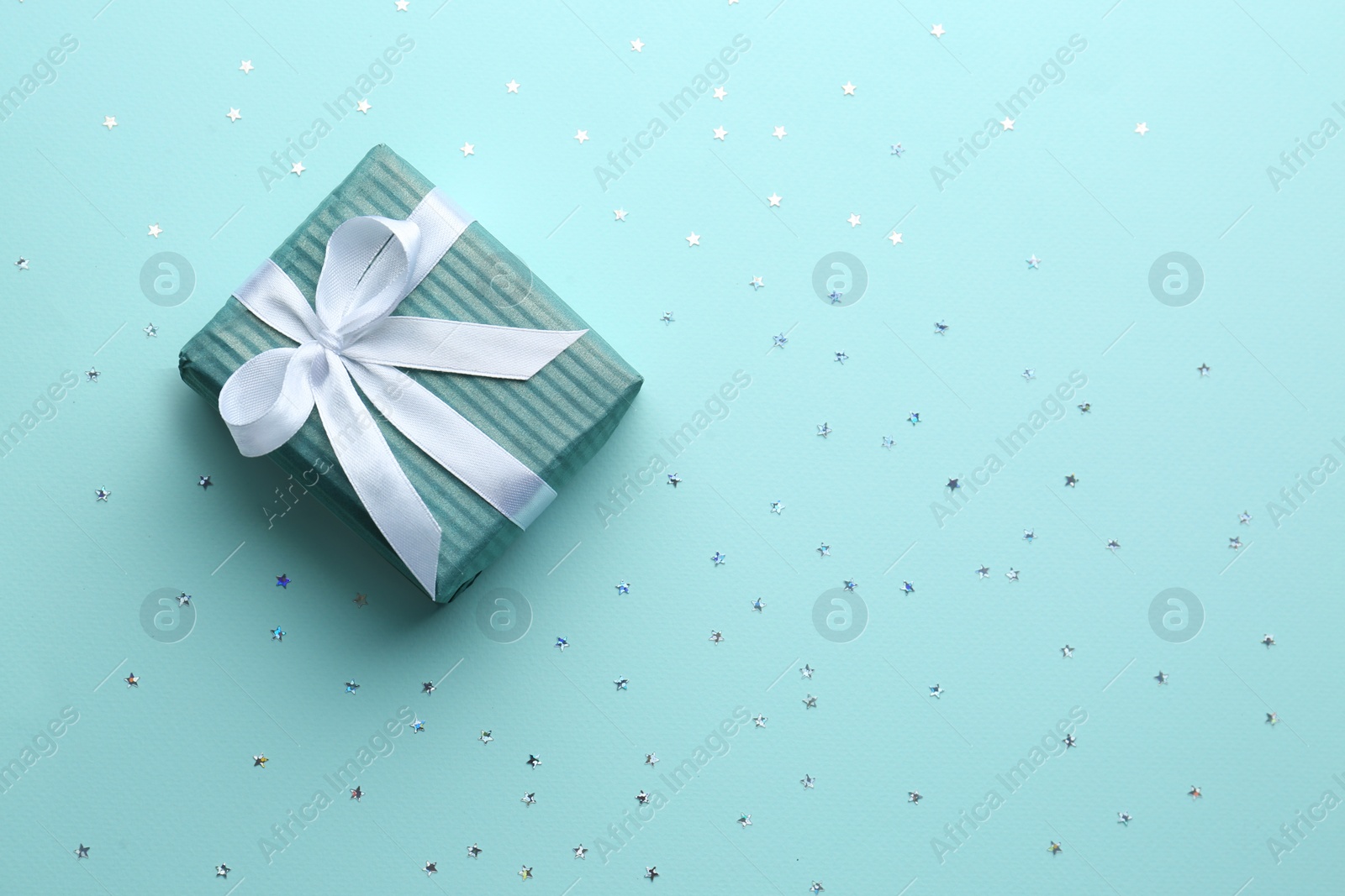 Photo of Gift box and confetti stars on light blue background, flat lay. Christmas celebration