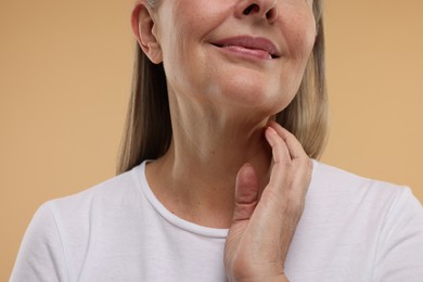 Mature woman touching her neck on beige background, closeup