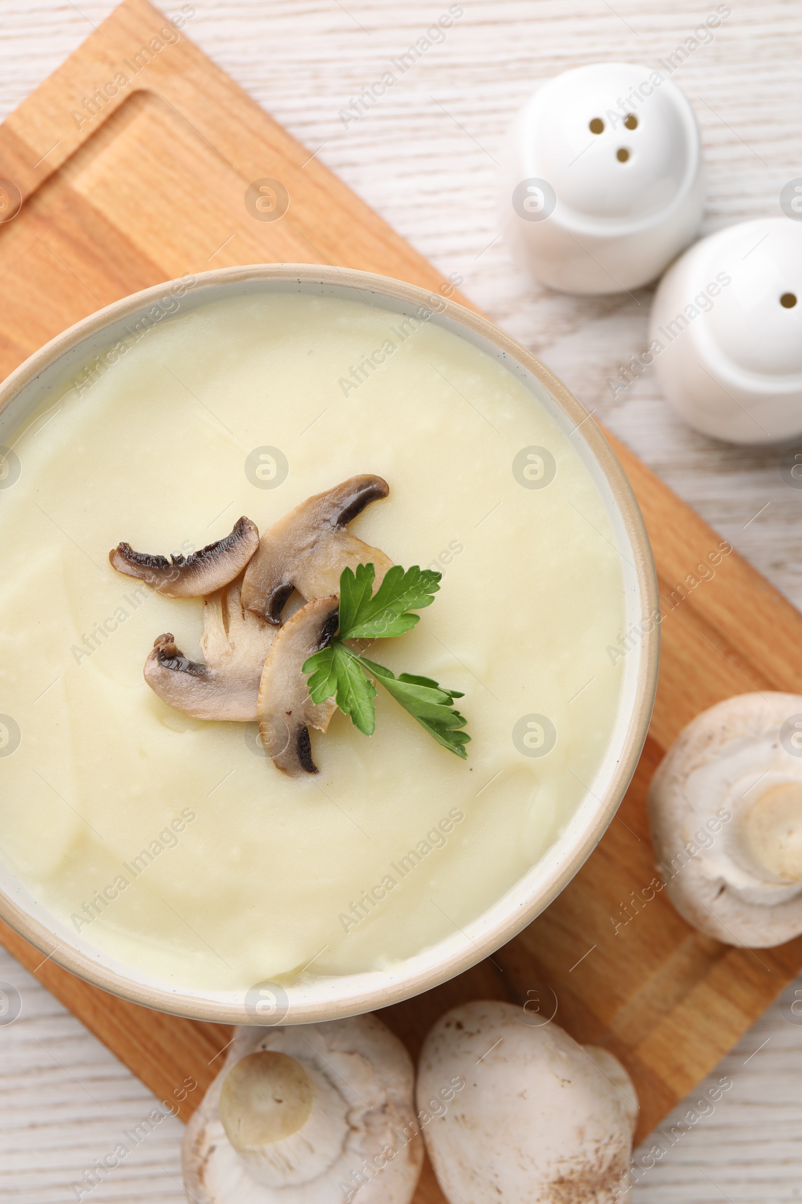 Photo of Bowl of tasty cream soup with mushrooms and parsley on light wooden table, flat lay