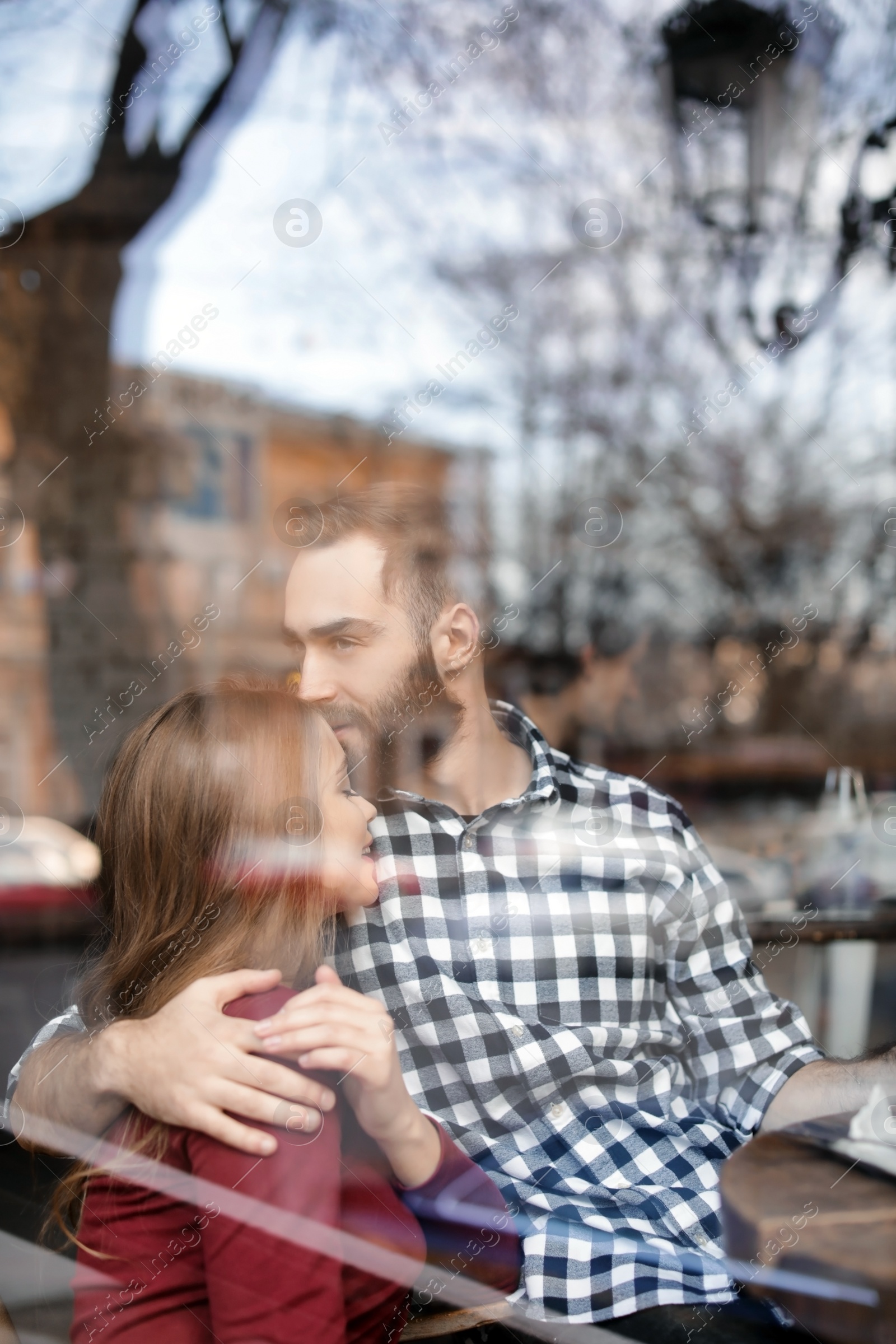 Photo of Lovely young couple spending time together in cafe, view from outdoors through window