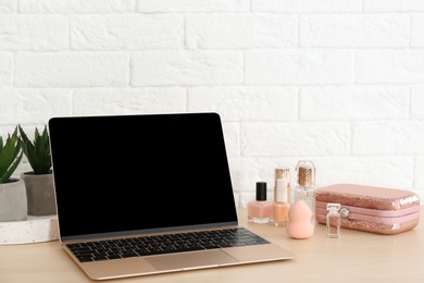 Photo of Stylish workplace with modern laptop and cosmetic products on table near brick wall, space for text. Beauty blogger