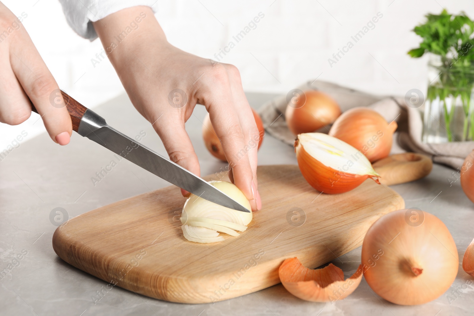 Photo of Woman cutting ripe onion at grey textured table, closeup