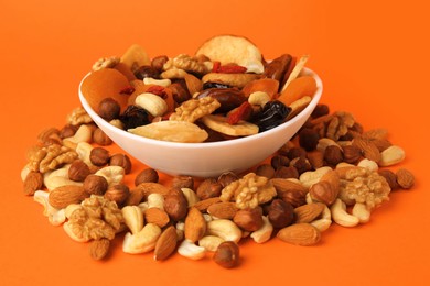 Photo of Bowl and mixed dried fruits with nuts on orange background, closeup