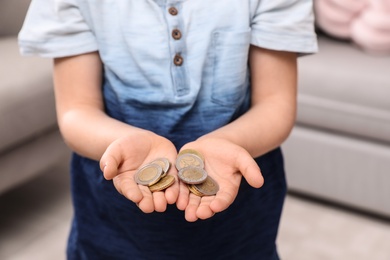 Photo of Little boy holding coins at home, focus on hands, closeup