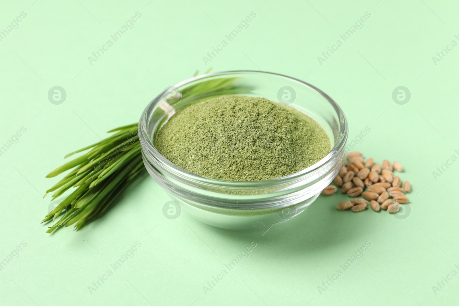 Photo of Wheat grass powder in bowl, seeds and fresh sprouts on green table