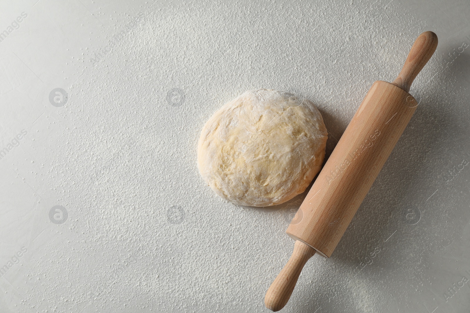 Photo of Raw dough and rolling pin on white table, top view. Space for text