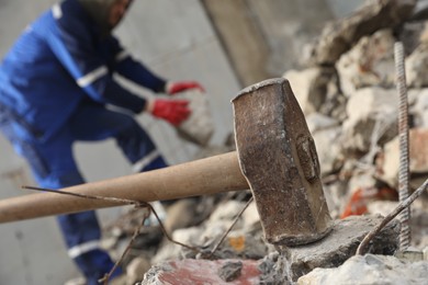 Photo of Sledgehammer on pile of broken stones. Man working outdoors, selective focus