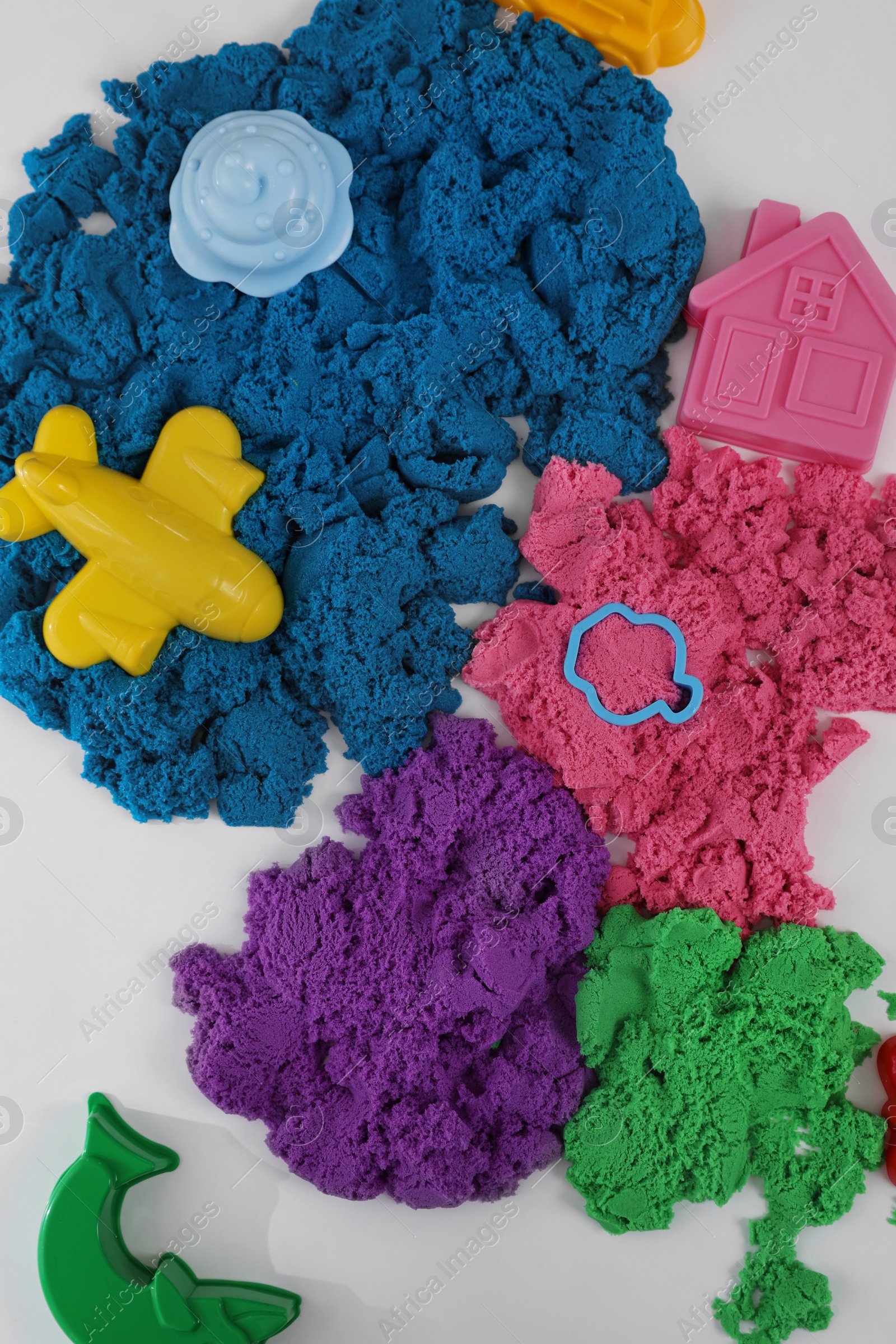 Photo of Bright kinetic sand and toys on white table, flat lay
