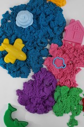 Bright kinetic sand and toys on white table, flat lay