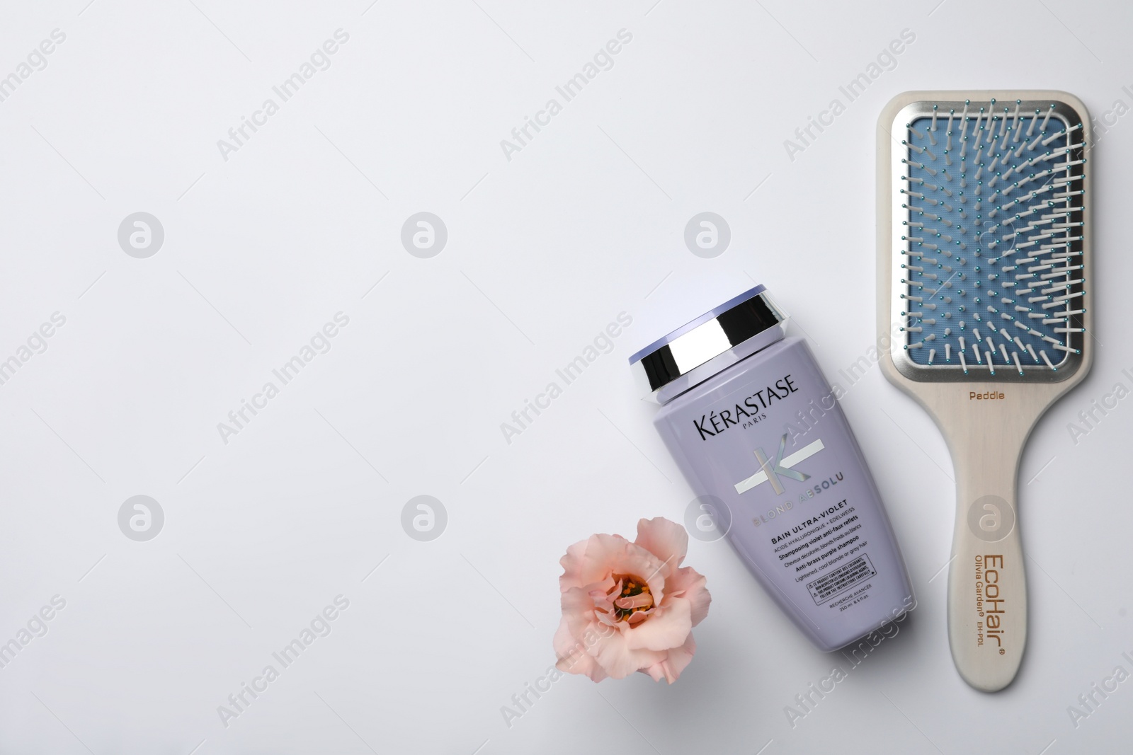 Photo of MYKOLAIV, UKRAINE - SEPTEMBER 07, 2021: Kerastase shampoo, hair brush and beautiful flower on light background, flat  lay. Space for text