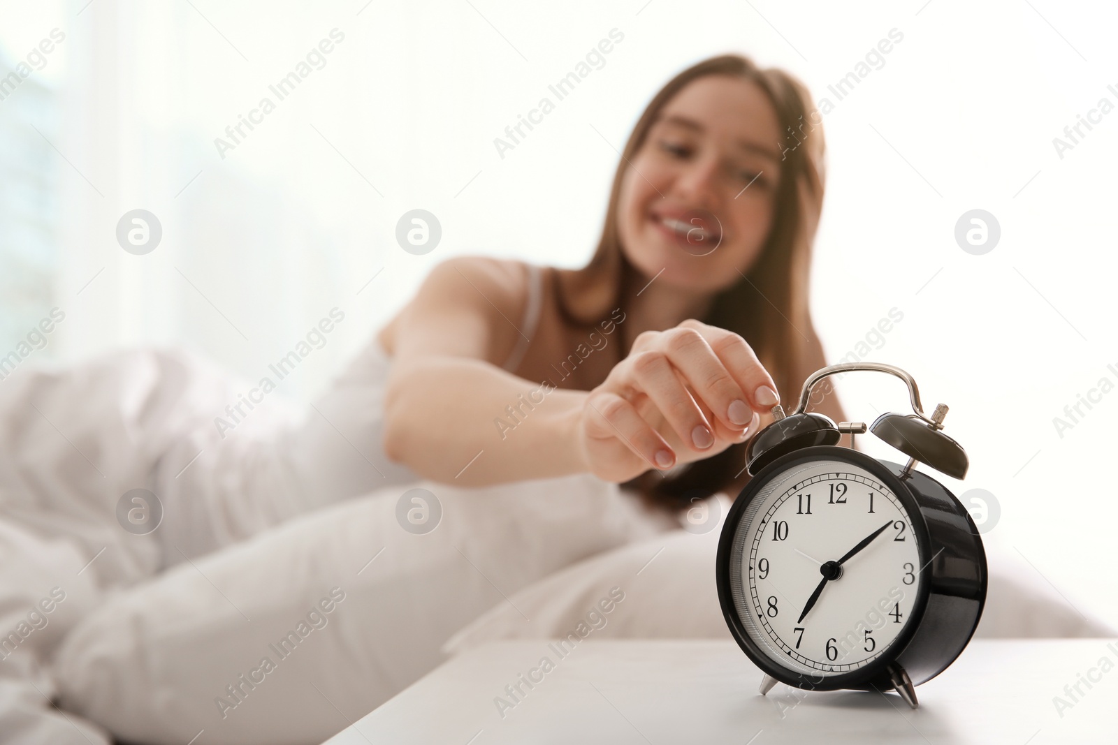 Photo of Young woman turning off alarm clock at home in morning, focus on hand