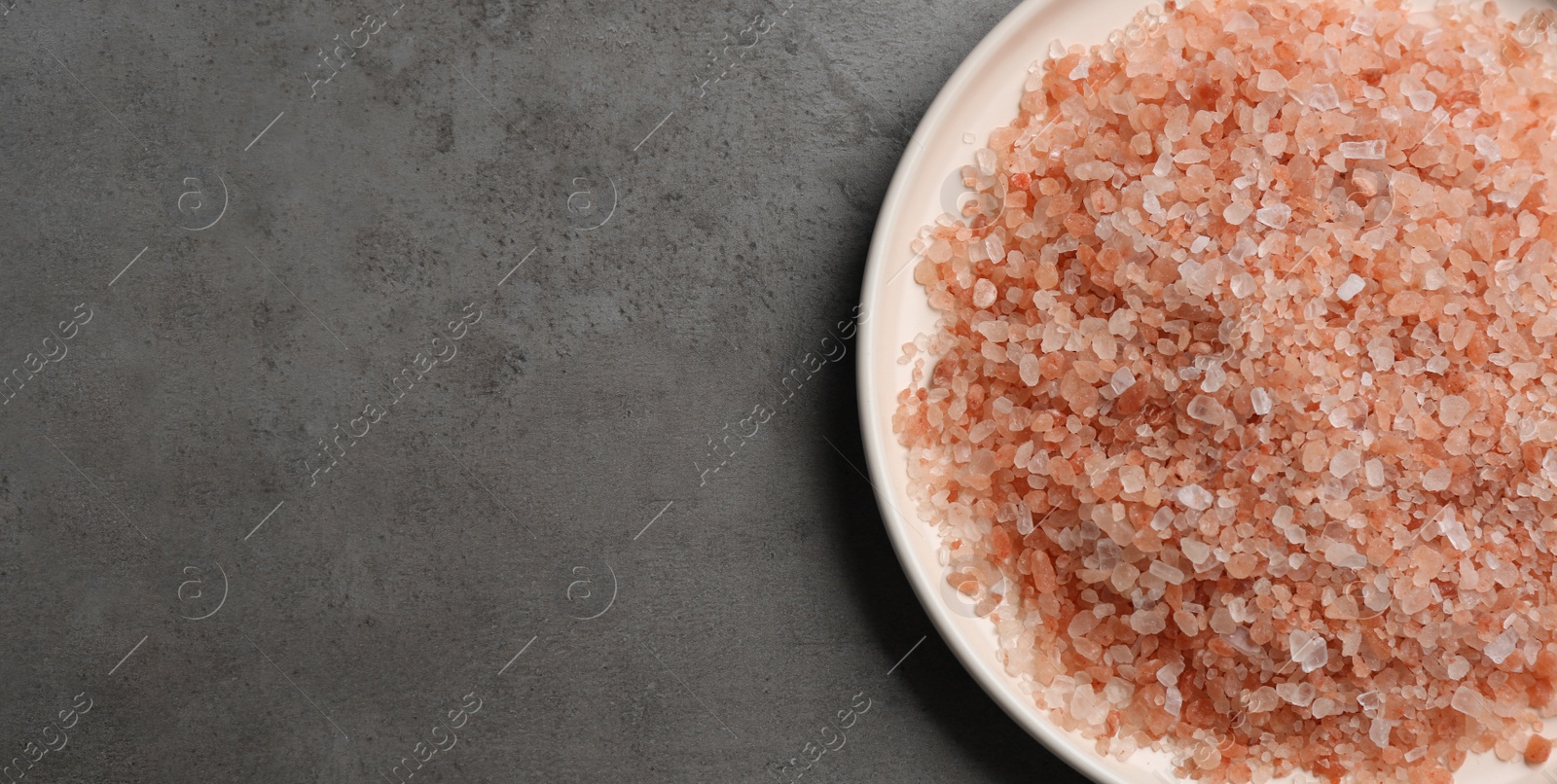 Photo of Pink himalayan salt on grey table, top view. Space for text