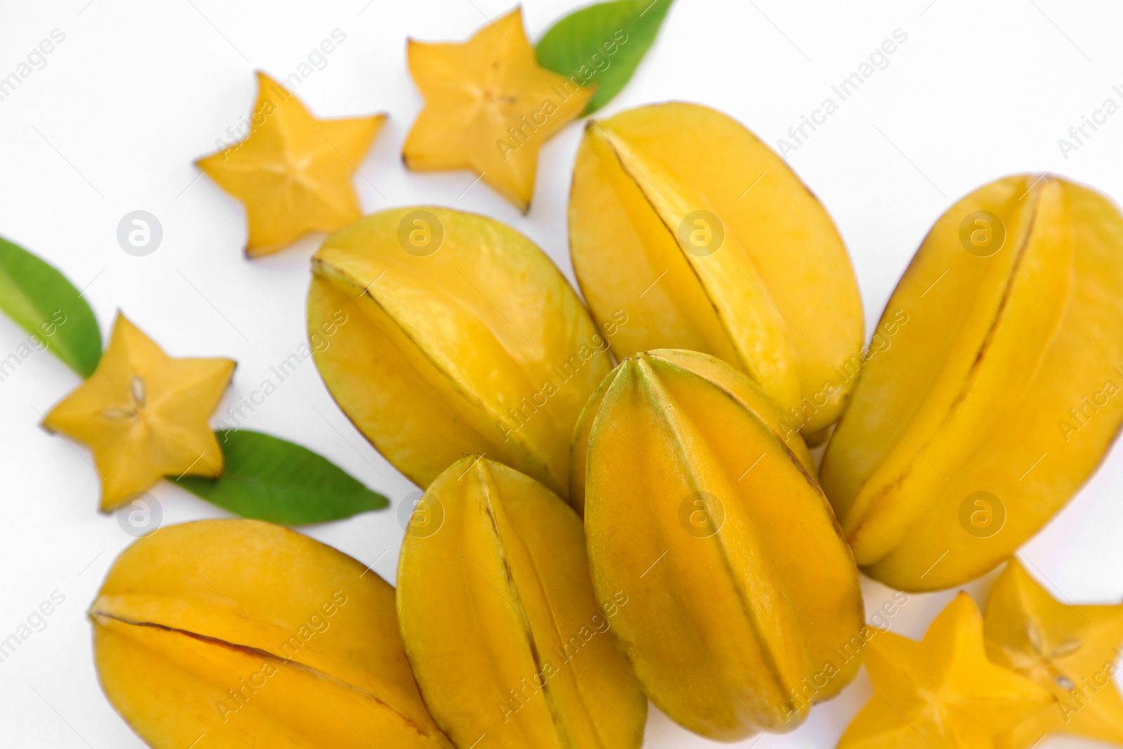 Photo of Delicious cut and whole carambolas with green leaves on white background, above view