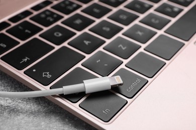 Photo of USB cable with lightning connector and laptop on grey table, closeup