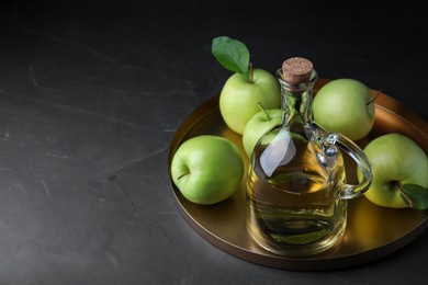 Fresh ripe green apples and jug of tasty juice on black table, space for text
