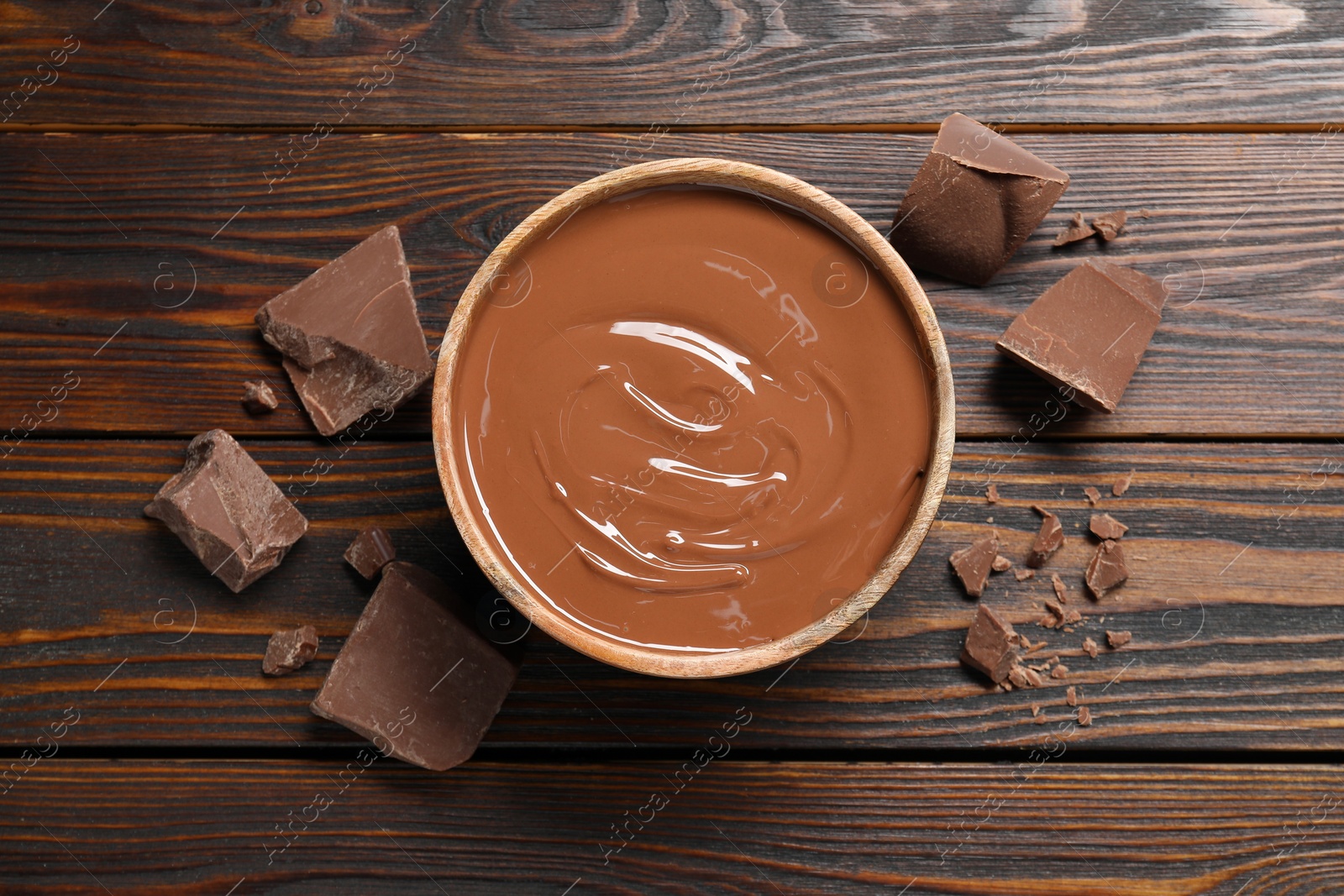 Photo of Tasty milk chocolate paste in bowl and pieces on wooden table, top view