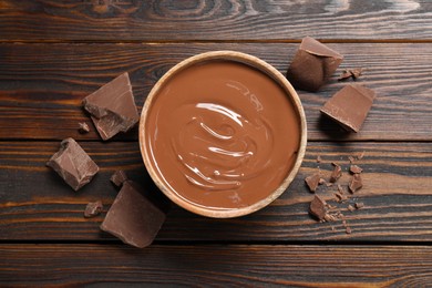 Photo of Tasty milk chocolate paste in bowl and pieces on wooden table, top view