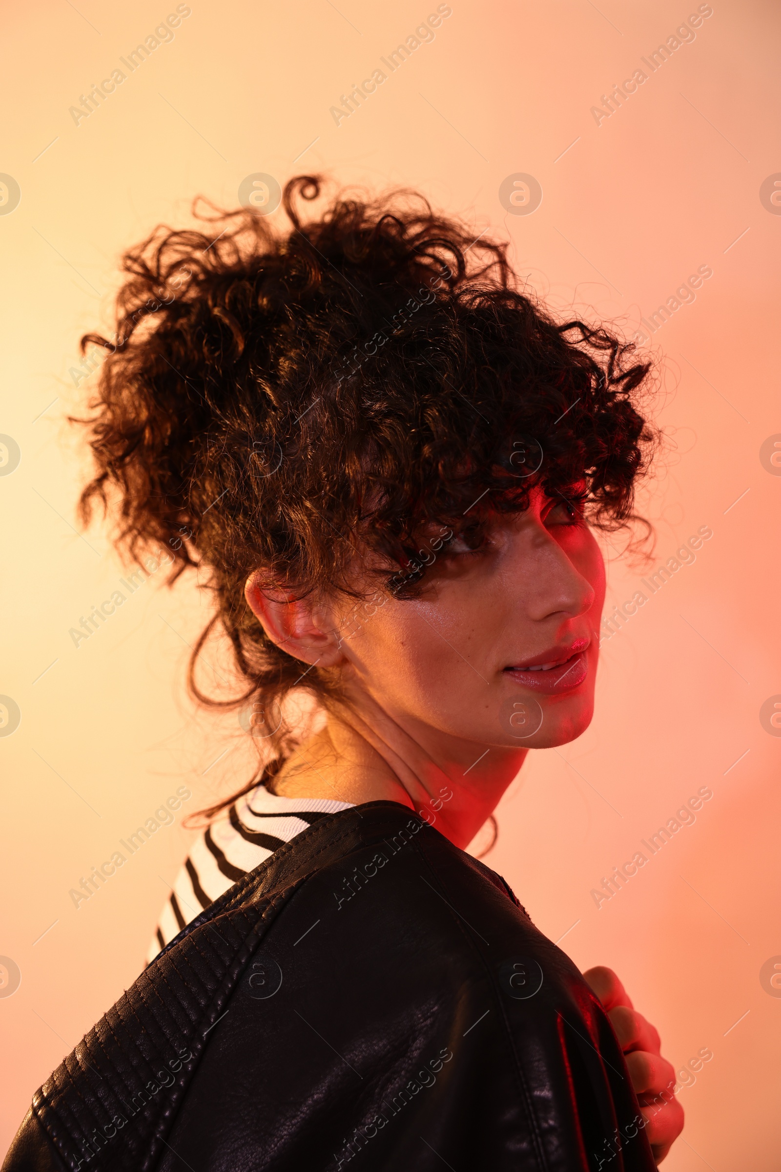 Photo of Beautiful young woman in black leather jacket posing on color background in neon lights