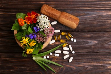 Photo of Mortar with fresh herbs, flowers and pills on wooden table, flat lay