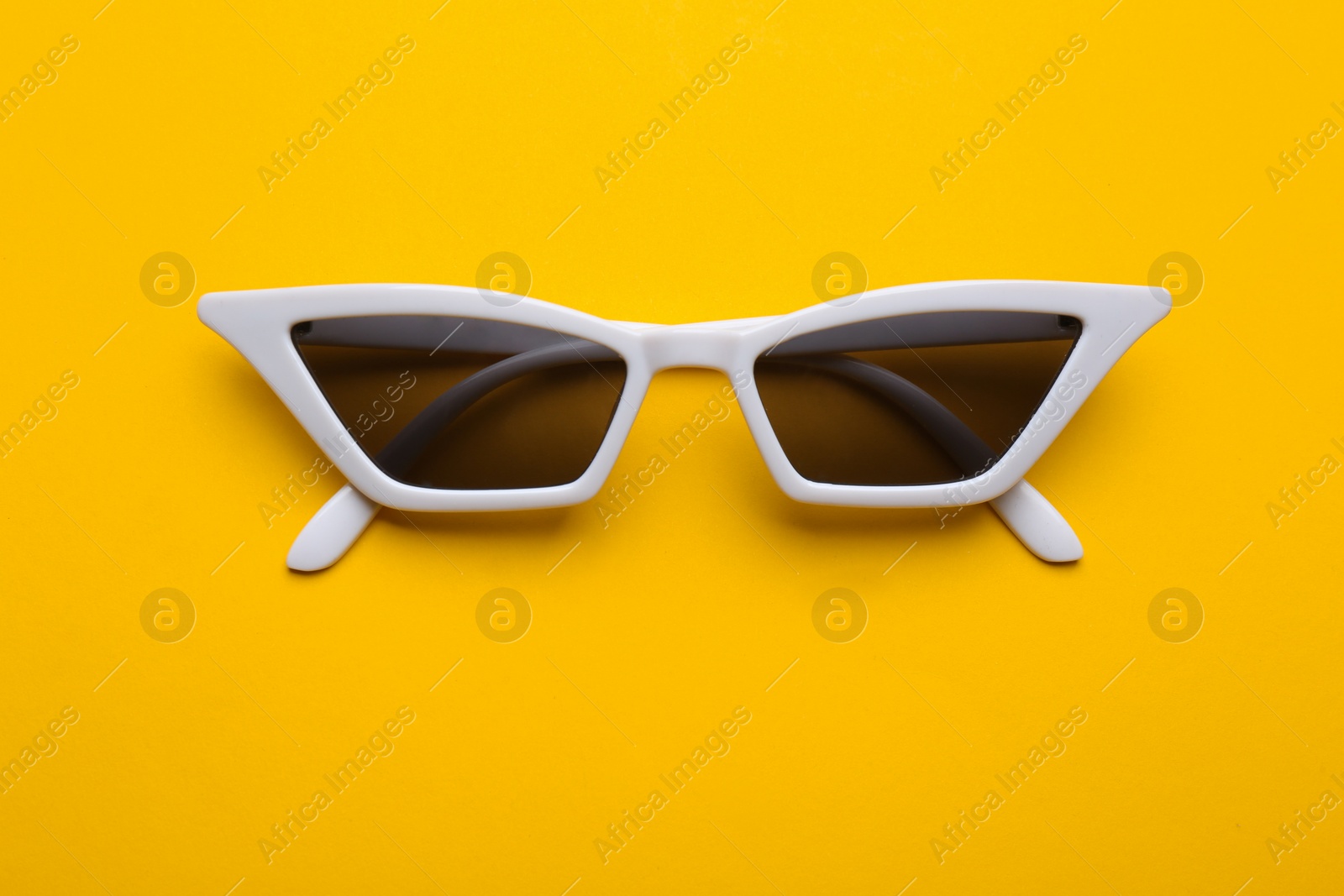 Photo of Stylish sunglasses on yellow background, top view. Fashionable accessory