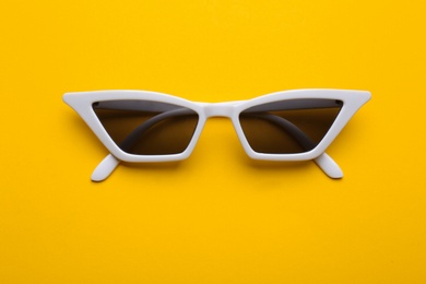 Photo of Stylish sunglasses on yellow background, top view. Fashionable accessory