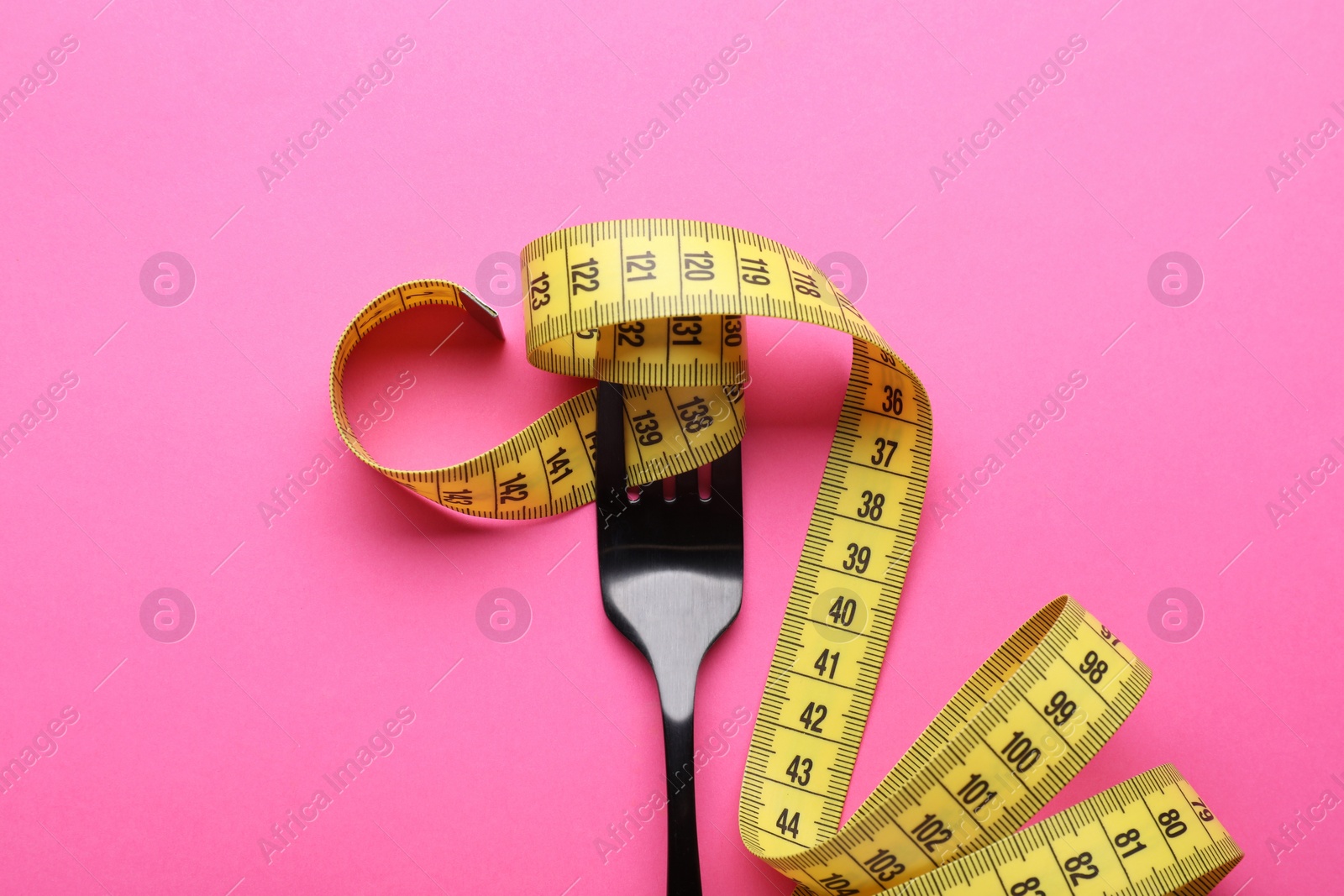 Photo of Fork with measuring tape on pink background, top view. Diet concept