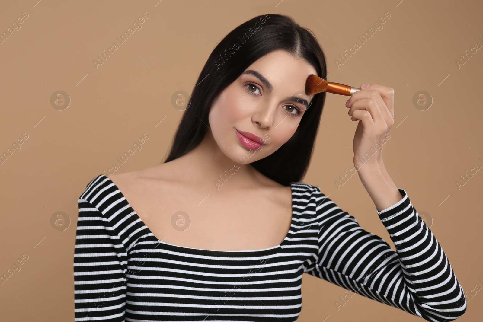 Photo of Beautiful woman applying makeup on light brown background