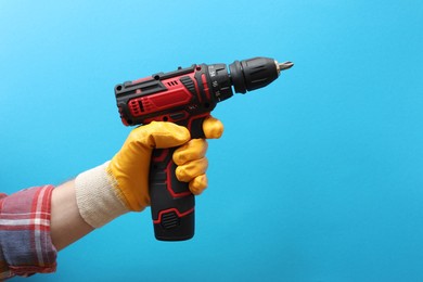 Photo of Handyman holding electric screwdriver on light blue background, closeup. Space for text