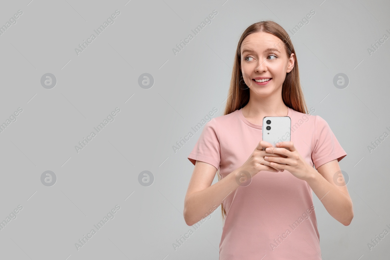 Photo of Happy woman sending message via smartphone on grey background, space for text