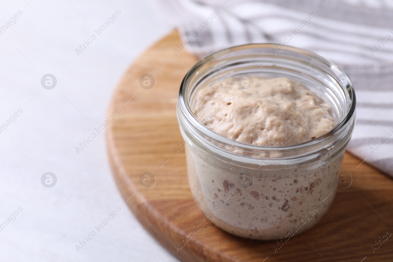 Photo of Sourdough starter in glass jar on light table, closeup. Space for text